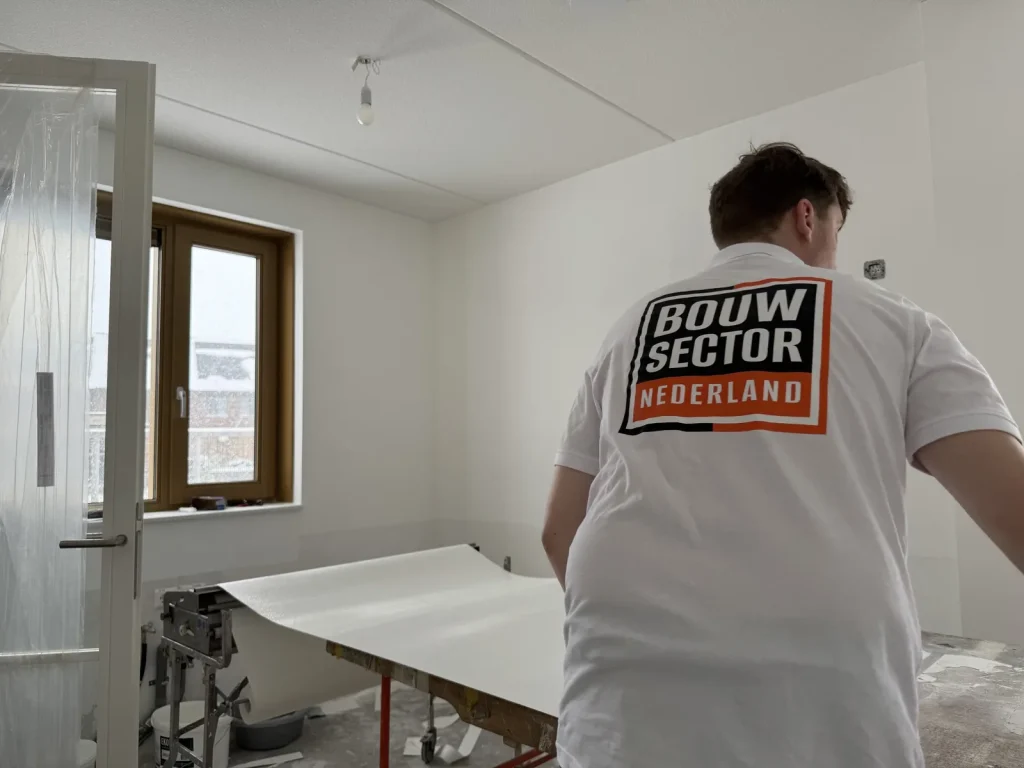 Behanger van Bouwsector Nederland bij de plaktafel met een baan vlies in een nieuwbouwkamer
