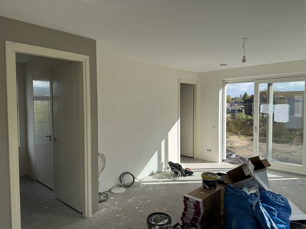 Nieuwbouwwoonkamer tijdens de afwerking, met een grijze en een witte wand en materiaal op de vloer