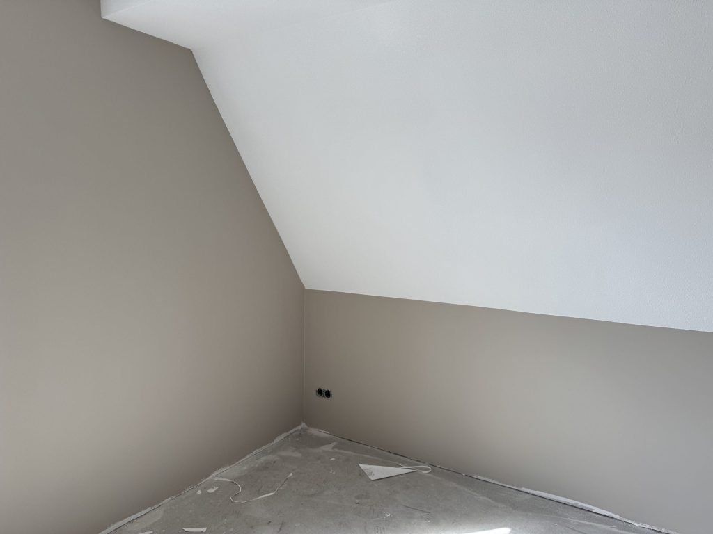 Zolderkamer met een schuine wand, onderste wanden in een warme grijstint en het schuine deel wit