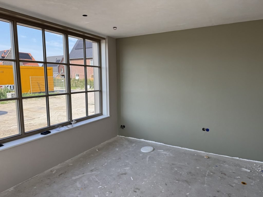 Nieuwbouwkamer met een grijsgroen geverfde wand naast een groot raam met roedes