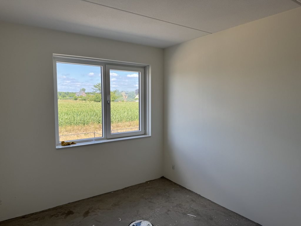 Lege kamer met strak afgewerkte lichte wanden en een raam met uitzicht op een maisveld