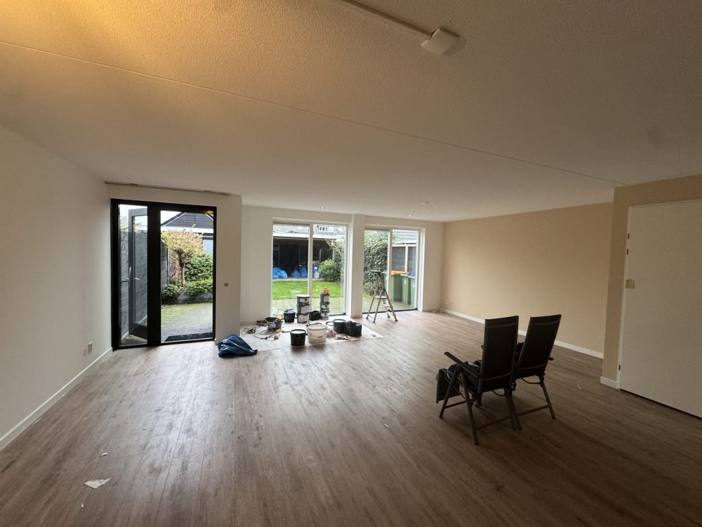 Woonkamer met lichte wanden en een houten vloer, verfspullen bij de tuindeuren