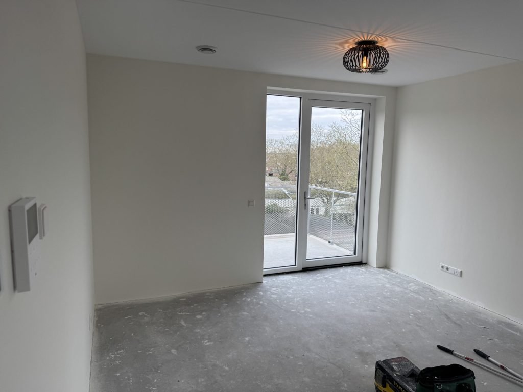 Lichte kamer met gladde witte wanden en openslaande deuren naar het balkon