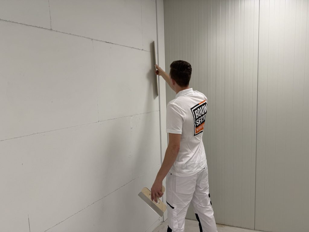 Stukadoor trekt een wand van gipsblokken af met een lange spaan